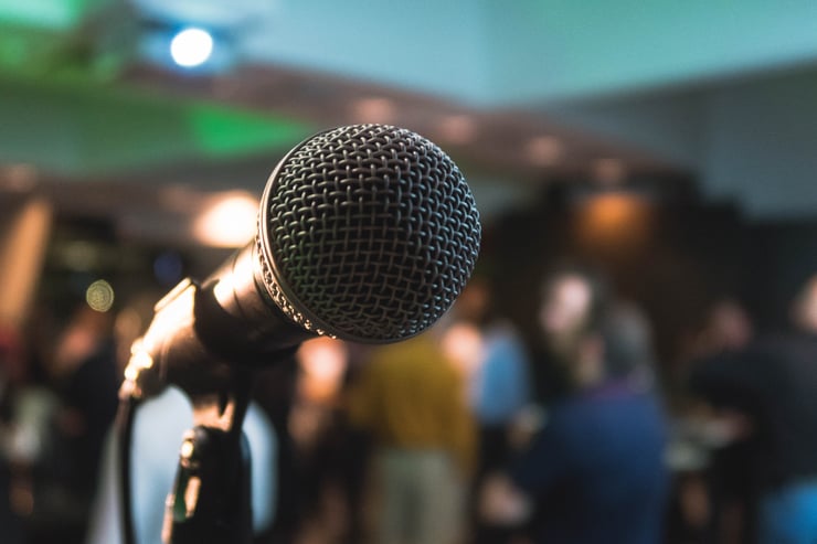 A close up shot of a microphone in front of a crowd. Photo by Kane Reinholdtsen courtesy of Unsplash
